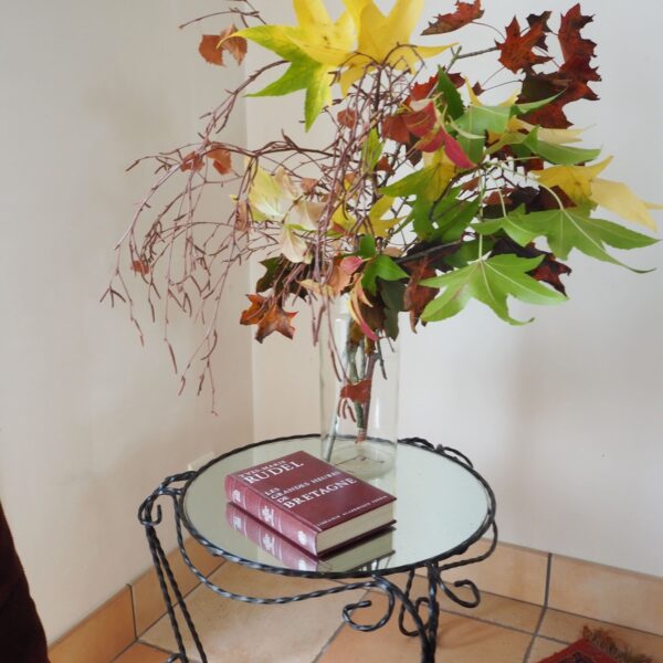 petite table basse en métal noir tourné et son plateau en miroir dans un décor d'automne